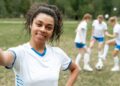 Footballeur souriant prenant un selfie, ses coéquipiers s'entraînant derrière lui.